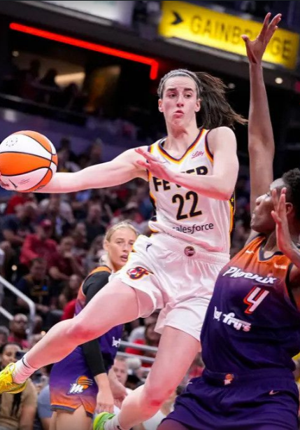 A woman in white and yellow basketball uniform jumping to catch the ball.